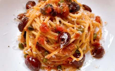 Ein Teller Spaghetti Puttanesca, garniert mit Oliven, Kapern und Parmesan.