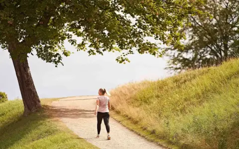 En kvinna går på en grusväg under ett träd. Hur lång tid tar det att gå en mil? Kanske en timme i detta vackra landskap.