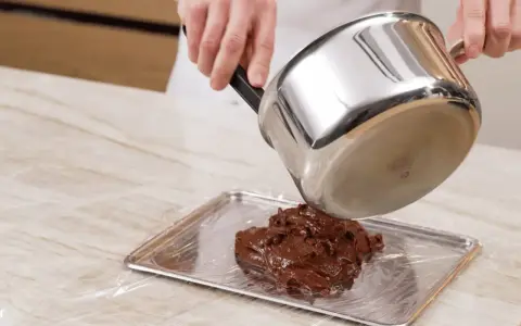 Comment faire fondre du chocolat : une casserole verse du chocolat fondu sur une plaque recouverte de film plastique.