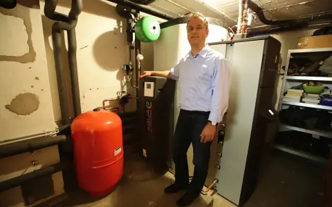 Mann steht neben Heizungsanlage, um Solarthermie zu optimieren. Roter Ausdehnungsbehälter und schwarze Wärmepumpe sichtbar.