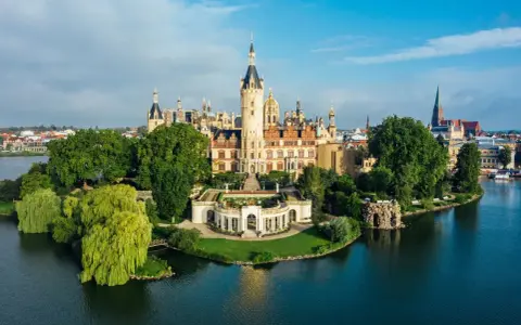 Schweriner Schloss auf einer Insel, umgeben von Wasser und grünen Bäumen. Ein Märchenschloss, das zu den Schwerin Geheimtipps zählt.