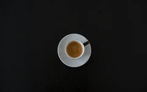 Czarna filiżanka espresso na białym spodeczku na ciemnym tle. Może symbolizować początek walki z objawami odstawienia kofeiny.