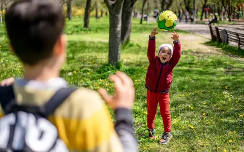 Un enfant joyeux lance un ballon en l'air dans un parc, un autre enfant est devant.