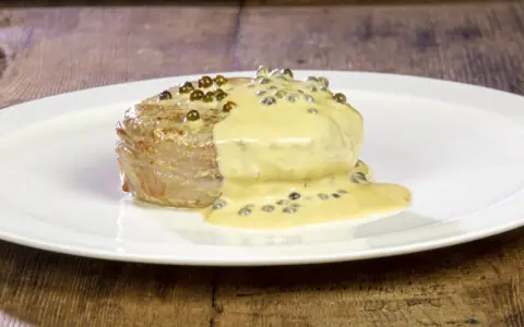 Un succulento filetto al pepe verde, ricoperto da una cremosa salsa, servito su un piatto bianco.