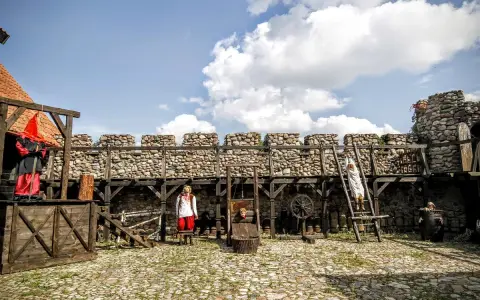 Scena z Muzeum Tortur w Krakowie: gilotyna, postacie w strojach historycznych i kamienne mury.