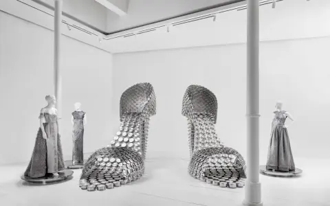 Installazione artistica mostra valentino roma: due enormi scarpe metalliche e abiti da sera su manichini.