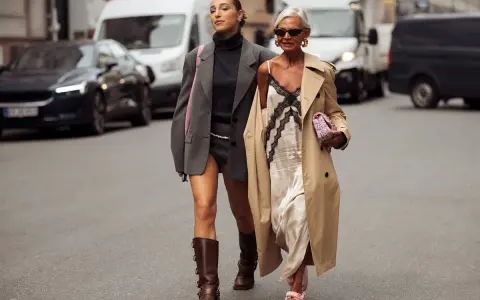 Dos mujeres pasean por la calle. Una lleva un vestido lencero de invierno con un abrigo y la otra un traje gris.