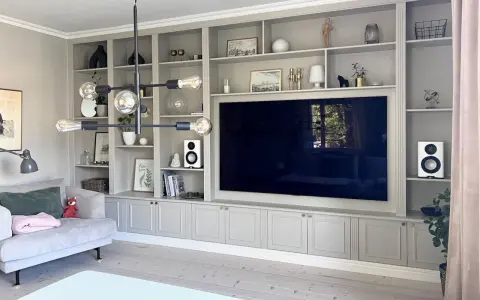En platsbyggd bokhylla i vardagsrummet med en stor TV i mitten. Hyllorna är fyllda med böcker, dekorationer och växter.