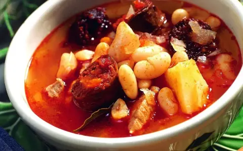 Un reconfortante plato de alubias con chorizo, trozos de morcilla y patatas en un caldo rojizo.