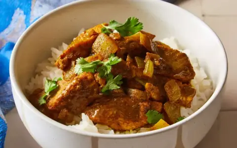 Aksamitny kurczak w sosie curry, podany na białym ryżu, z gałązkami kolendry. Idealny prosty przepis na obiad.