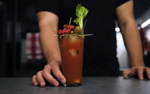 Bloody Mary na soku pomidorowym kontra na passacie. W szklance drink z lodem, ozdobiony oliwkami, suszonym pomidorem, kiełbaską i selerem.