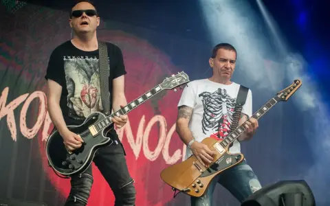Dwóch gitarzystów na scenie, jeden w czarnej koszulce z sercem, drugi w białej z żebrami. Kocham cię jak Irlandię, grają rocka.