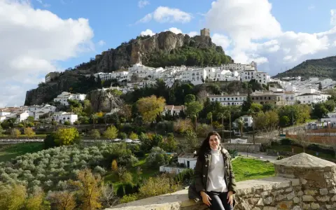 Una mujer sonríe ante el pintoresco pueblo blanco de la sierra de Cádiz, coronado por un castillo.