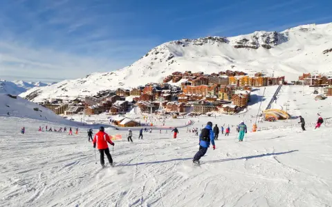 Ośrodek narciarski we francuskich Alpach. Tłumy narciarzy i snowboardzistów na stoku, w tle zabudowania. Francja narty gdzie najlepiej? Tutaj!