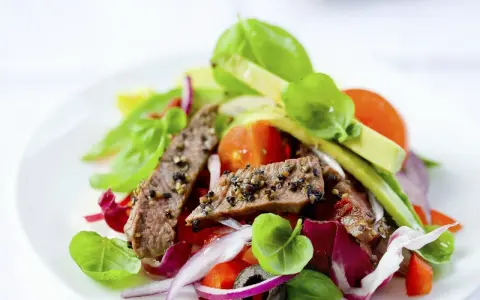 Frischer Salat mit zarten Rinderstreifen, Tomaten, roten Zwiebeln und Basilikum auf einem weißen Teller.