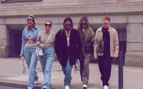 Fünf Freunde spazieren lässig, alle tragen Jeans. Welche Jeans sind in? Weite Schnitte und helle Waschungen dominieren den Look.