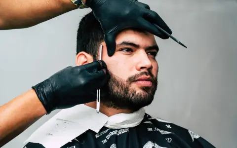 Barber precyzyjnie goli zarost brody ostrym narzędziem.