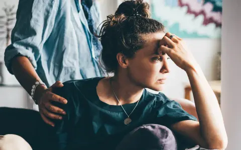 Una donna pensierosa, con una mano sulla fronte, riceve un gesto di conforto. Potrebbe riflettere sull'attaccamento evitante e la sessualità.