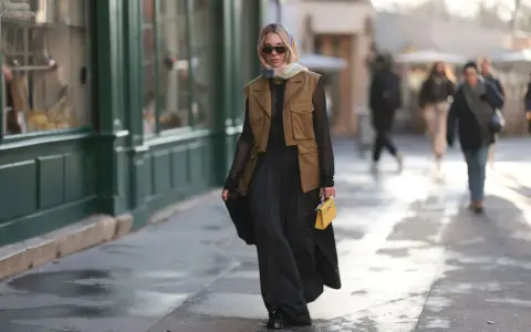 Mujer con chaleco negro corto, falda larga negra y bolso amarillo.