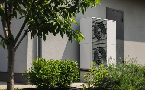 Nowoczesna pompa ciepła 3 5 kw, dyskretnie umieszczona przy ścianie domu, otoczona zielenią, zapewnia ekologiczne ogrzewanie.