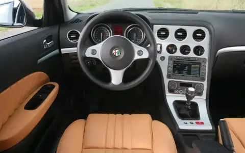 Wnętrze Alfa Romeo 159 1.9 JTD z beżową skórzaną tapicerką, kierownicą i konsolą środkową.