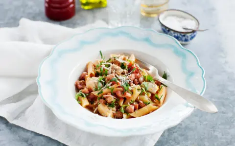 En tallrik med penne pasta, kyckling och tärnad pancetta, toppad med persilja och parmesan. Ett enkelt pancetta recept för en god middag.