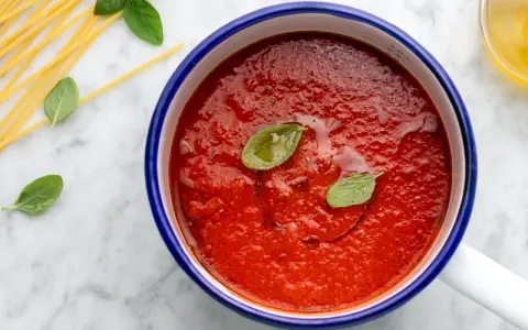 Sugo con pomodorini freschi, basilico e spaghetti crudi su marmo.