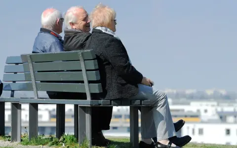 Trzech seniorów siedzi na ławce, rozmawiając. Może to dyskusja o tym, czym jest emerytura pomostowa i jakie daje możliwości.