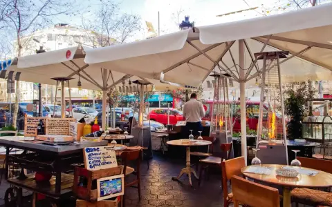 Terrasse d'un restaurant à Barcelone, avec des tables, des parasols, des chauffages d'extérieur et des panneaux indiquant des plats typiques espagnols.