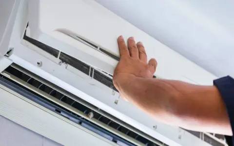 Main d'un technicien ouvrant un climatiseur pour vérifier l'eau et le filtre.