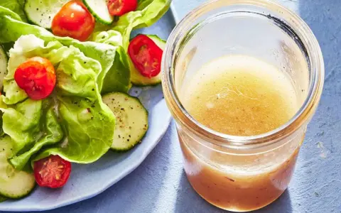 En burk med gyllene dressing till sallad står bredvid en fräsch sallad med sallad, gurka och tomater.