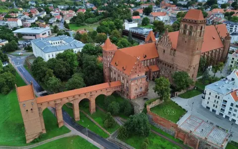Zamek w Kwidzynie, z charakterystycznym gdaniskiem i mostem, otoczony zielenią i zabudowaniami. Ciekawostki o zamku czekają na odkrycie!
