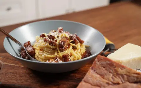 Miseczka spaghetti carbonara z boczkiem i parmezanem, obok kawałki sera i boczku.