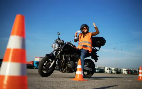 Szczęśliwa motocyklistka z prawem jazdy kategorii A3 w ręku, siedząca na motocyklu, świętuje sukces na placu manewrowym.