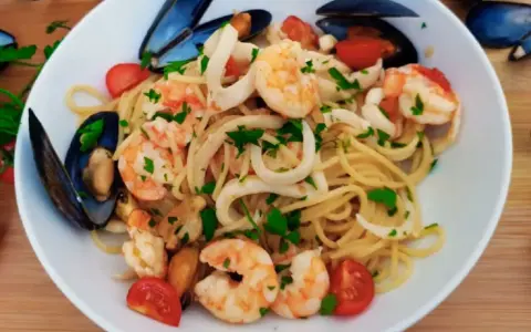 Pyszne Linguine Frutti di Mare przepis: makaron z krewetkami, kalmarami i małżami, udekorowany pomidorkami i natką pietruszki.