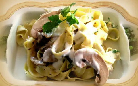 Pyszne tagliatelle z grzybami w kremowym sosie, udekorowane natką pietruszki.
