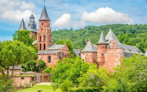 Magnifique ensemble de bâtiments en pierre rouge, dont une église romane et des tours, au milieu d'une végétation luxuriante. Idéal pour découvrir que faire autour de Rocamadour.