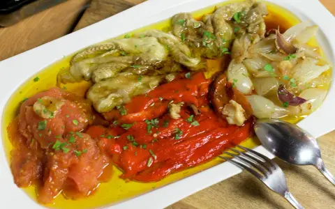 Deliciosa escalivada al forn con pimientos rojos, berenjenas, tomates y cebollas asadas, regada con aceite de oliva y perejil picado.
