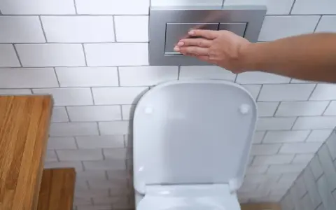 Mano presionando el botón de descarga de una cisterna empotrada, un ejemplo de los modernos tipos de cisternas wc.