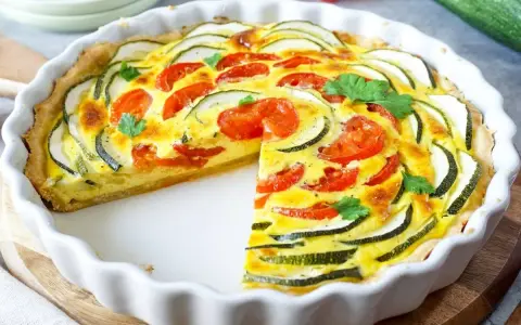 Eine köstliche Zucchini-Quiche mit Tomaten und frischer Petersilie, in einer weißen Quicheform serviert.