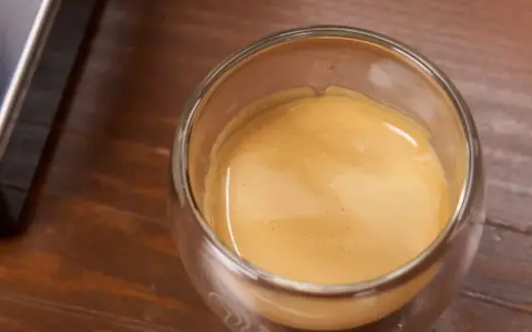 Ein Glas Espresso mit einer feinen Crema auf einem Holztisch. Ein kleiner Schuss Sahne macht den Kaffee mit Sahne gesund und lecker.