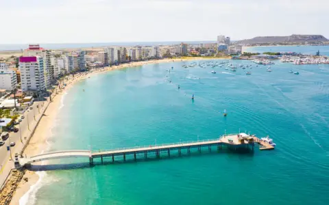 Malecón w Manta, Ekwador. Widok na plażę, budynki, molo i zatokę z łodziami. Tu właśnie leży Ekwador, kraj na równiku.
