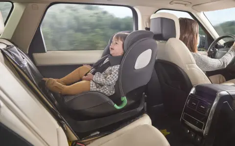 Bebé sonriente en silla de coche a contramarcha, viajando segura mientras mamá conduce.