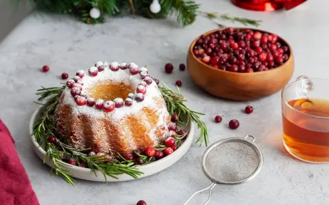 En vackert dekorerad sockerkaka med lingon och rosmarin, perfekt för julfika tips. En skål med lingon och en kopp te fullbordar julstämningen.