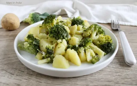 Un plato de brócoli con patatas, sencillo y saludable. Una patata entera y trozos de brócoli reposan cerca.