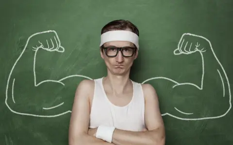 Chudy mężczyzna w okularach i opasce na głowie, z narysowanymi po bokach bicepsami, jakby po zażyciu omnadren 250.