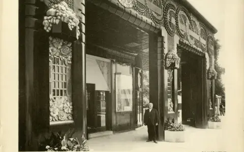 Façade de galerie de boutiques, style art déco, avec ornements floraux et motifs circulaires. Un homme en costume se tient sur le trottoir.