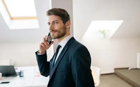 Mężczyzna w garniturze rozmawia przez telefon, jego wyraz twarzy sugeruje, że nastąpiła **zmiana głosu podczas rozmowy**.