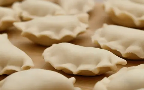 Surowe pierogi z jagodami leżą na drewnianej desce, gotowe do gotowania.