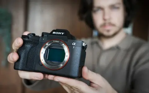 Mężczyzna trzyma aparat Sony Alpha z widocznym obiektywem i mocowaniem E-mount.